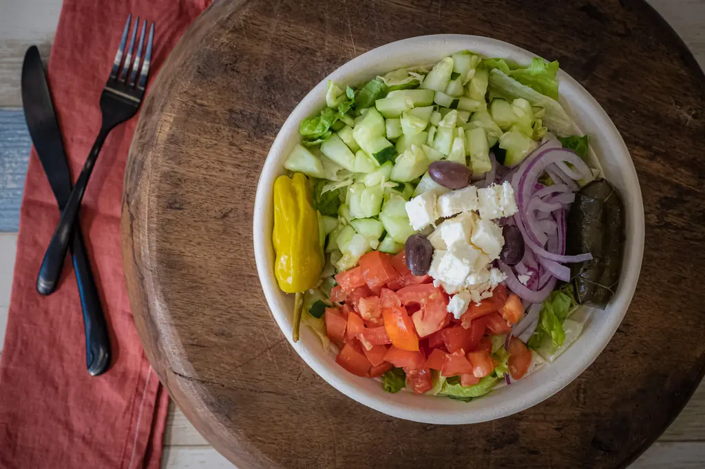 Greek salad with feta, olives, tomato and pepperoncini served on a wooden table